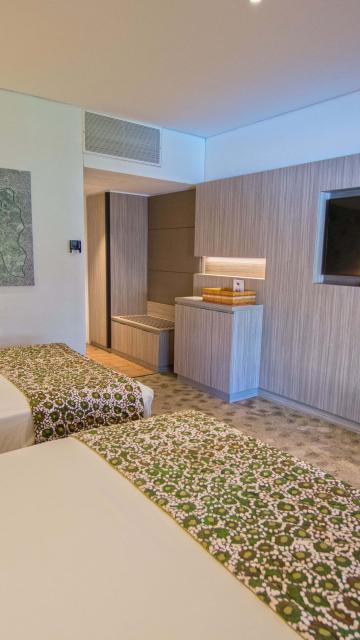 Two double beds in modern hotel room with tv on wall