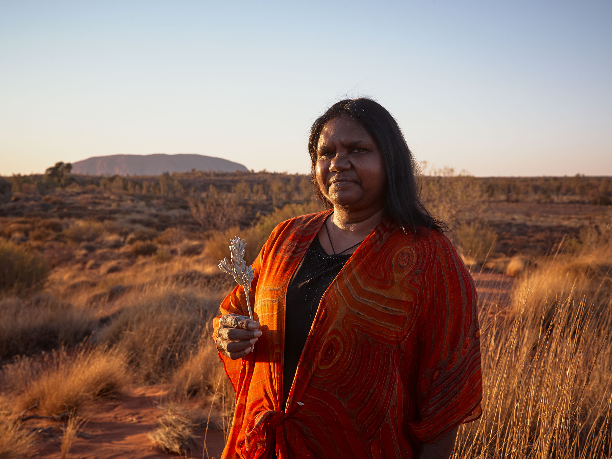 An Anangu woman holds a flower with Uluru in the background