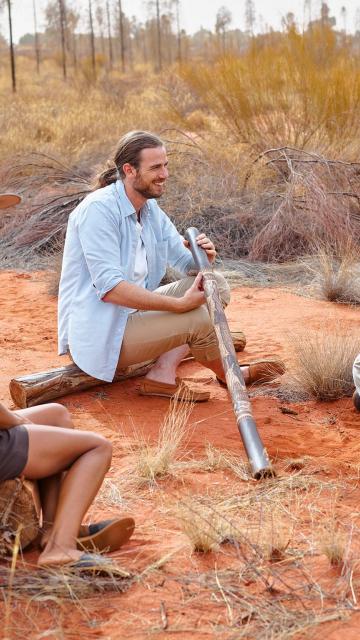 Man in outback learning to play didgeridoo
