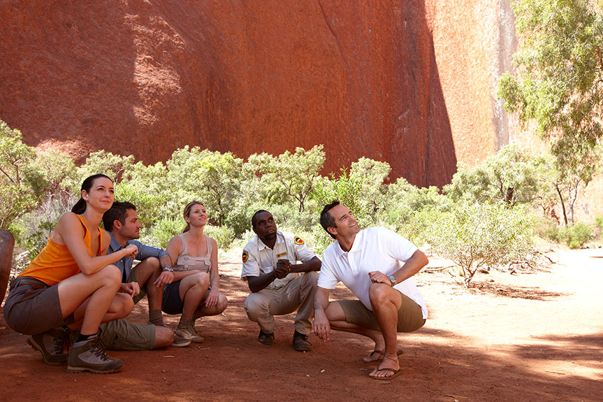 people crouching in the shadow of Ayers Rock
